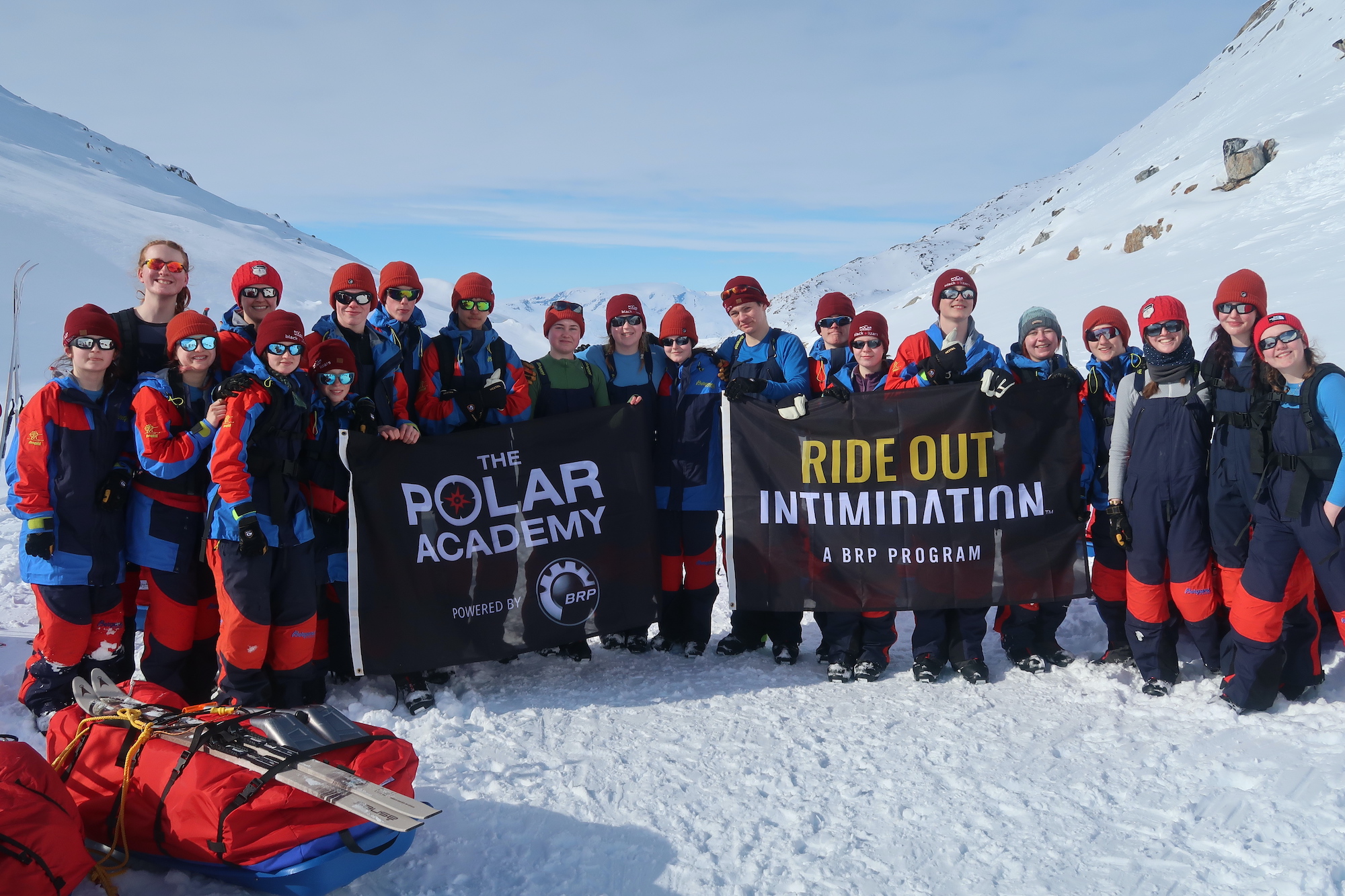 The young people of the 2023 Expedition on the ice in Greenland all together holding up flags with the BRP logo and smiling